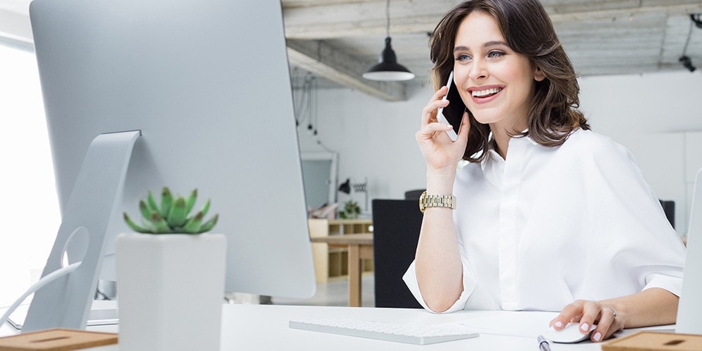 A woman talks on the phone while using her computer